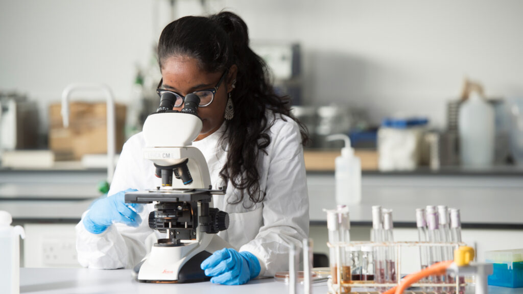 A young black researcher looking through microscope.