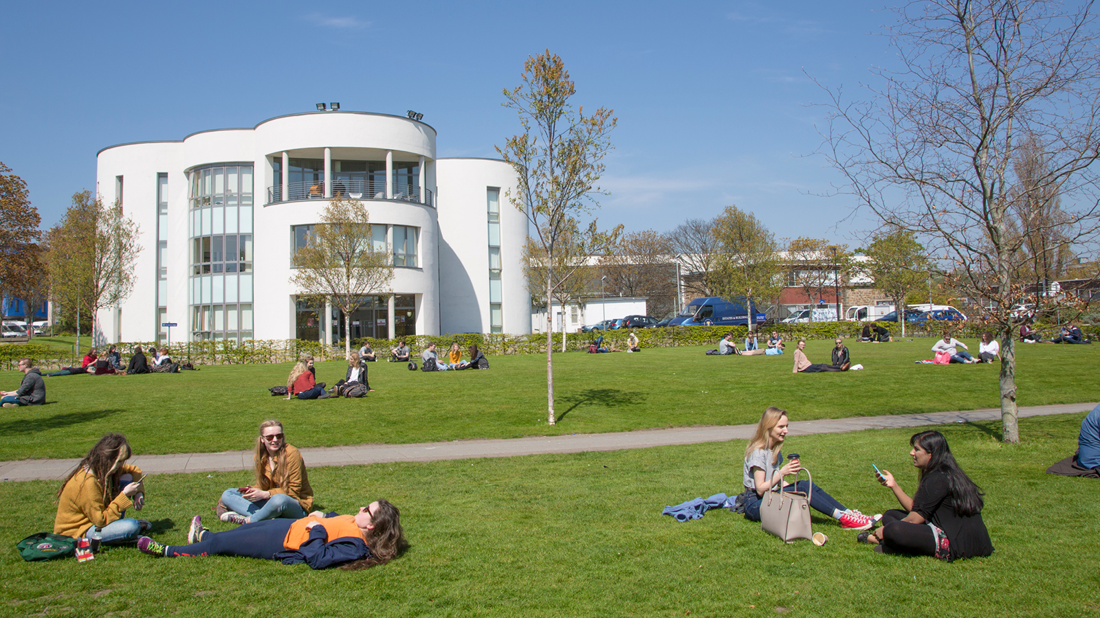 Different groups of students sitting by the sun on the University of Dundee Campus.