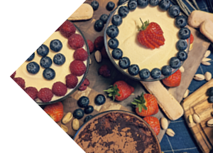 Top view of desserts arranged on a wooden surface, including tiramisu with blueberries and strawberries, and various cookies and nuts scattered around.